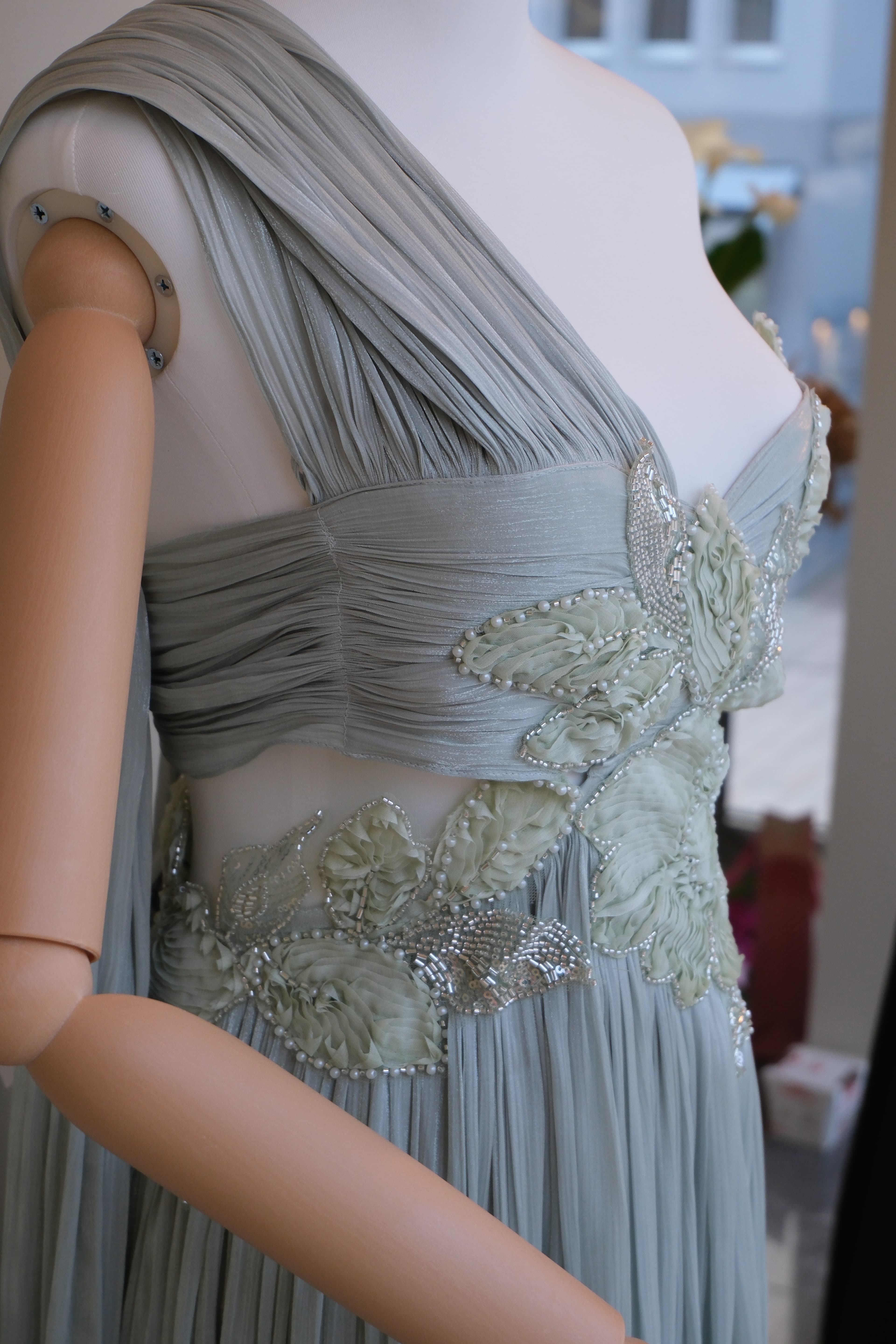 Close-up of hand-stitched crystal and floral beading at the hip of the pleated sage gown